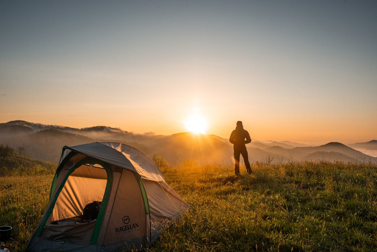 Man standing in open field at sunrise with tent